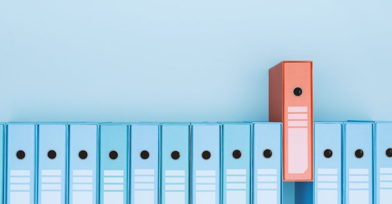 A row of blue ring binders with one orange binder standing out