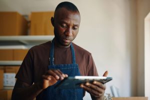 Business owner in an apron checking figures on a tablet in his stockroom