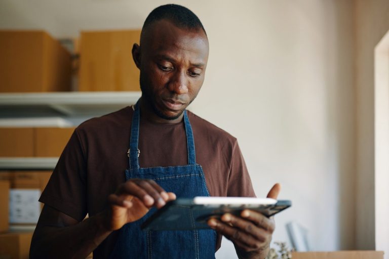 Business owner in an apron checking figures on a tablet in his stockroom