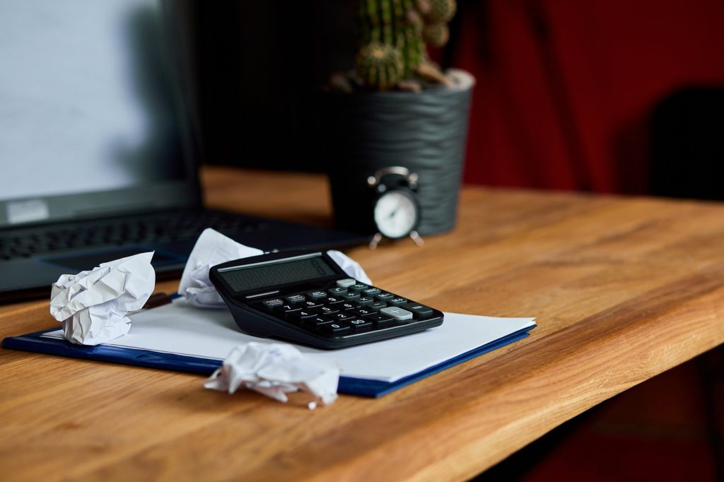Calculator, crumpled paperwork and a clock on a wooden desk before a tax deadline
