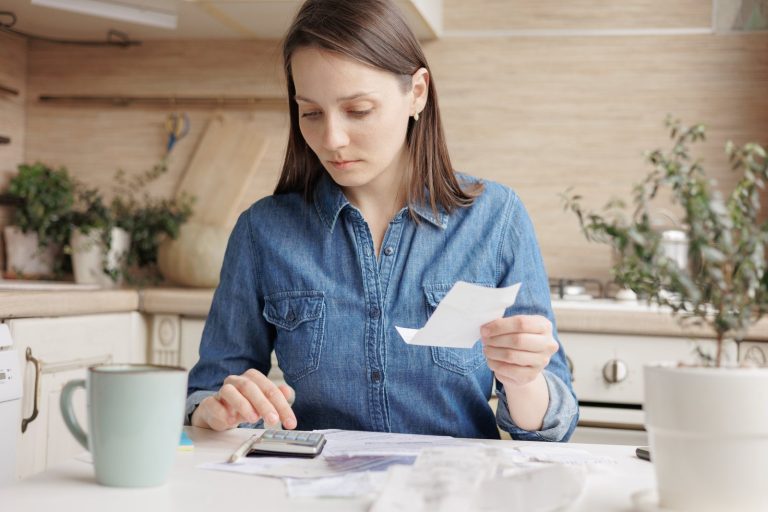 Self-employed woman checking receipts with a calculator at her kitchen table