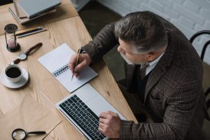 Business owner writing notes beside a laptop and coffee on a wooden desk