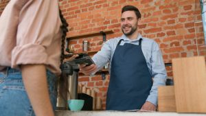 Smiling coffee shop owner taking a card payment from a customer